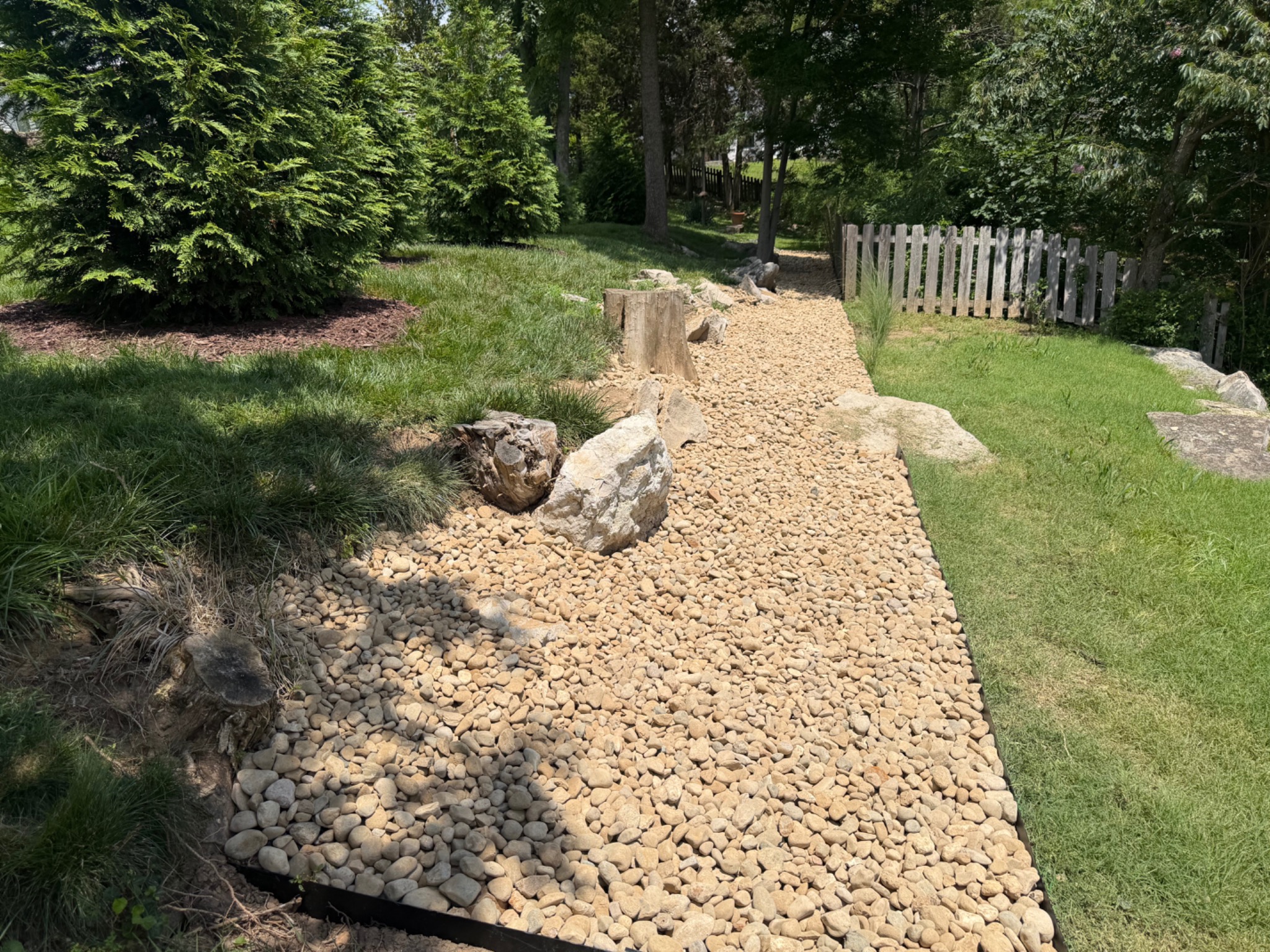 Decorative river rock landscape installation along a wooded residential path