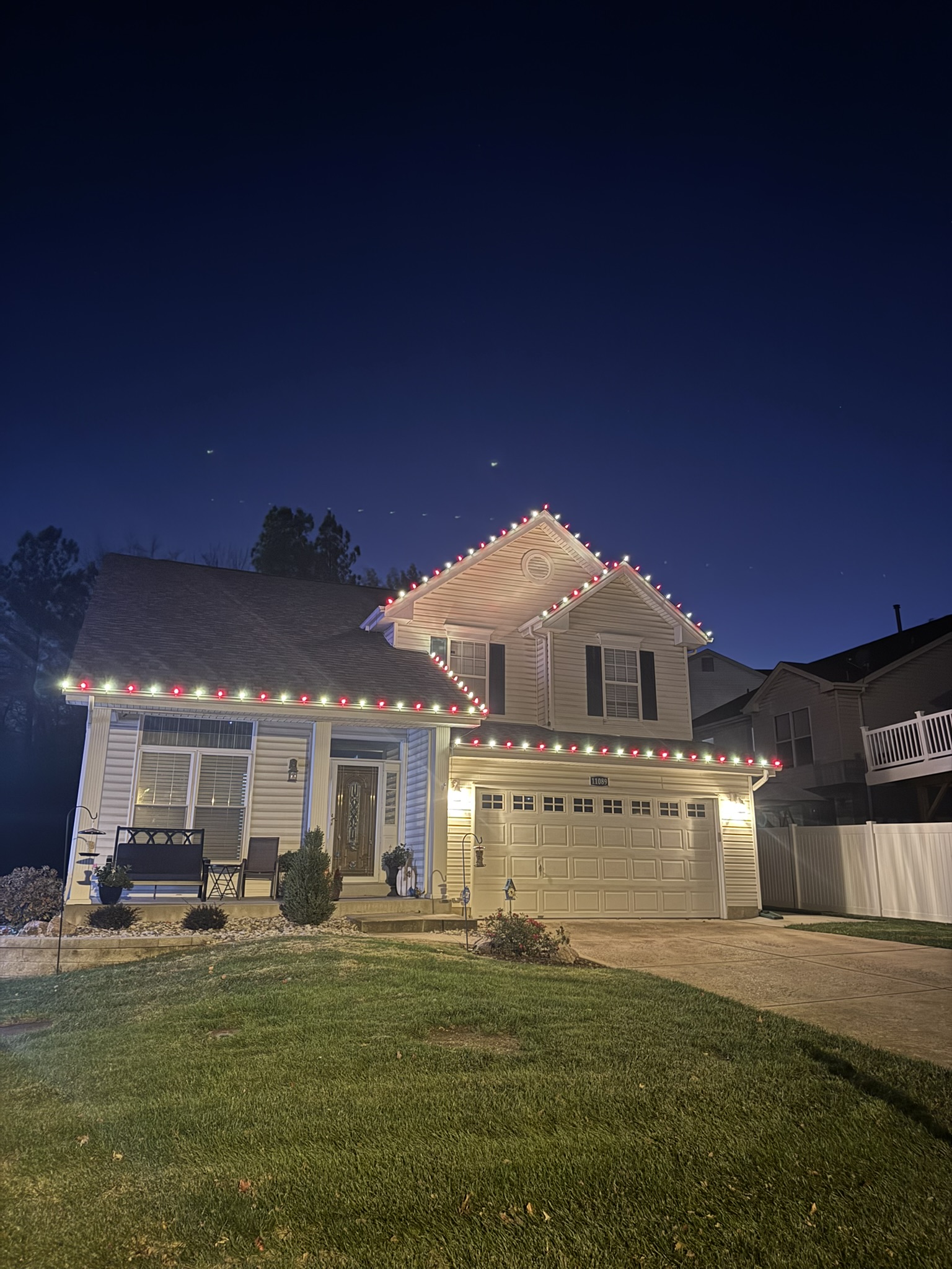 Red and white holiday lights outlining the front roofline of a two-story home at dusk.