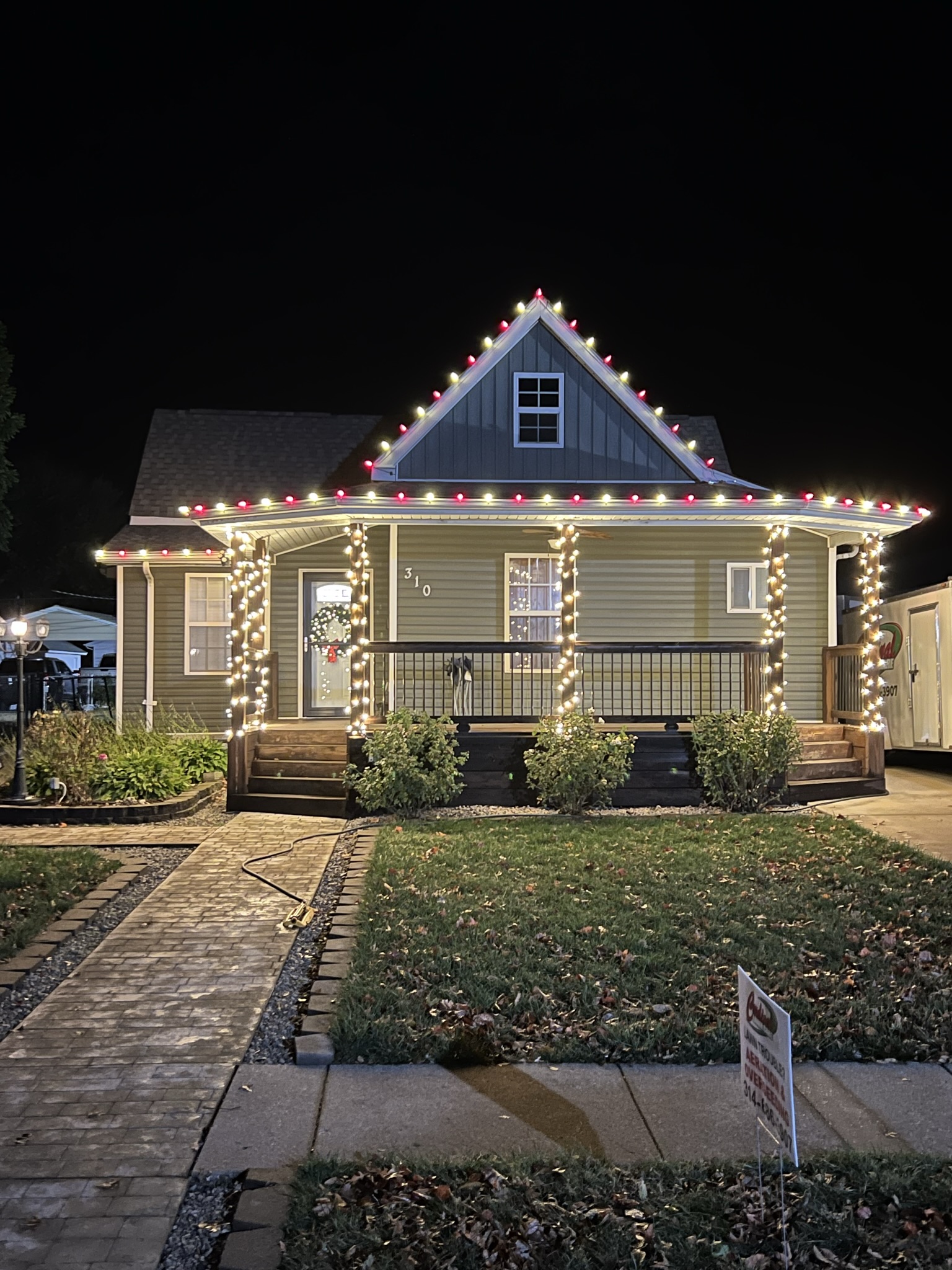 Red and white roofline lighting with warm white lights wrapped around porch posts.