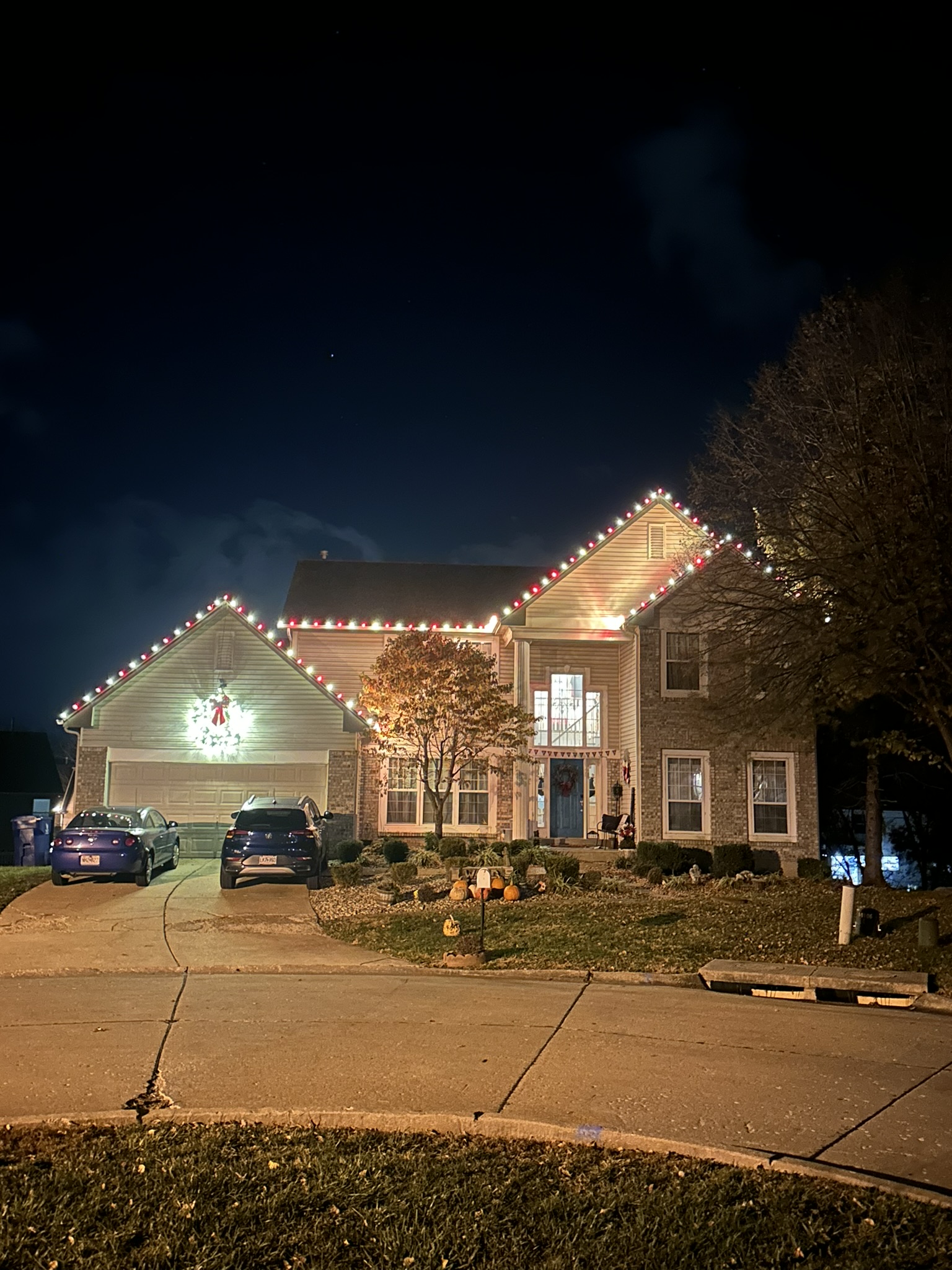 Red and white lights outlining a two-story home's roofline, with an illuminated wreath above the garage.